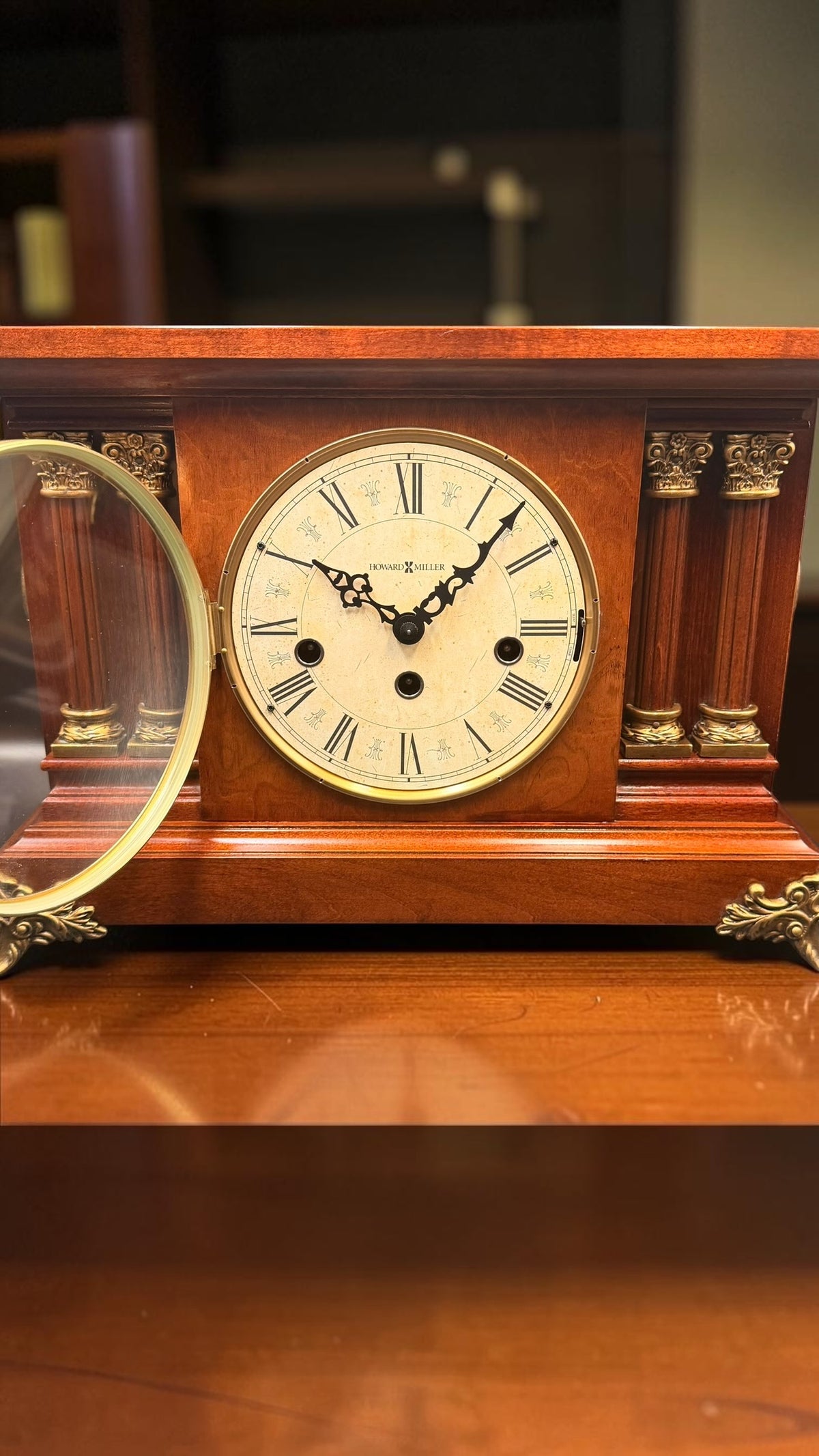 Open brass-rimmed hinged glass door of Howard Miller Circa mechanical clock