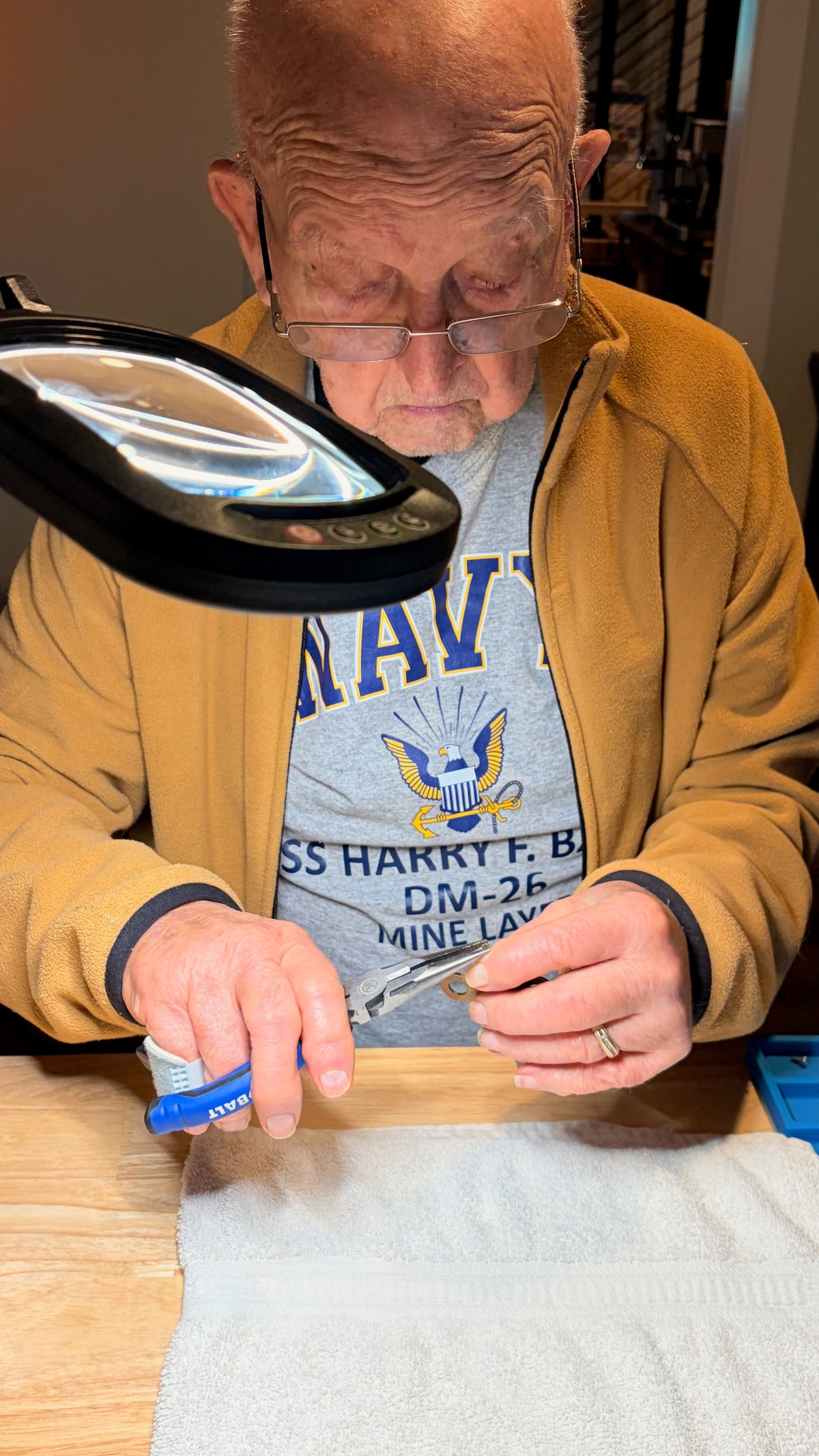 Andy’s dad assisting with a small clock component under a magnifying lamp.