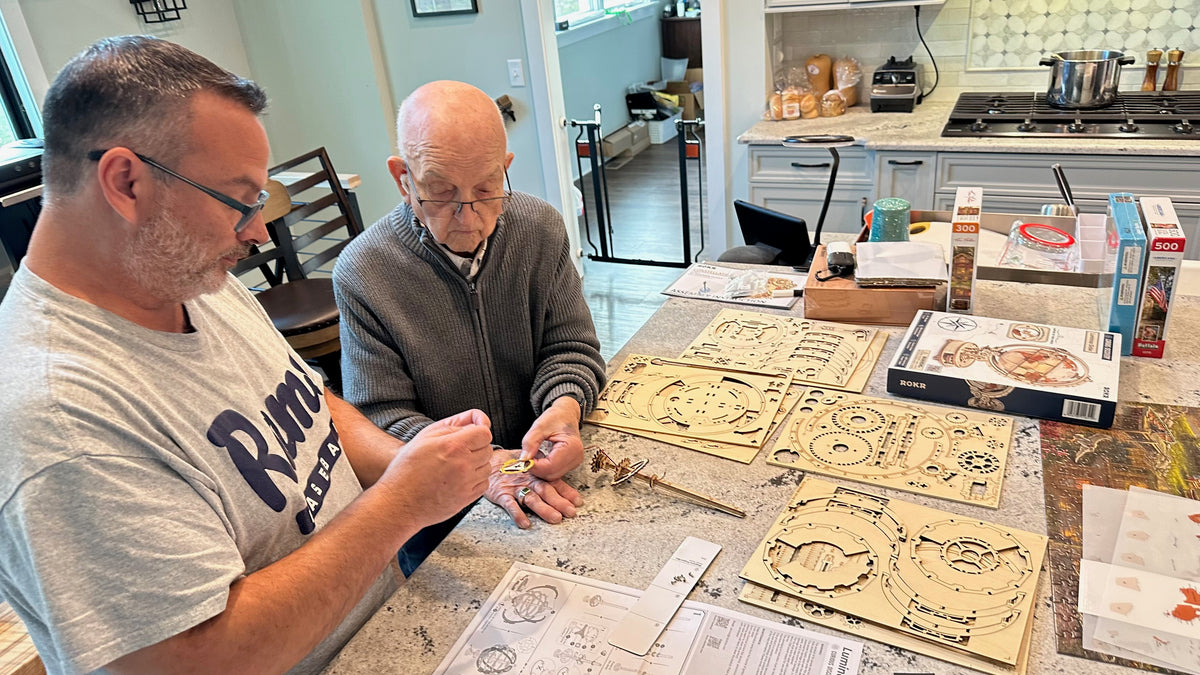 Andy and his dad working together on a wooden clock model at the kitchen counter.