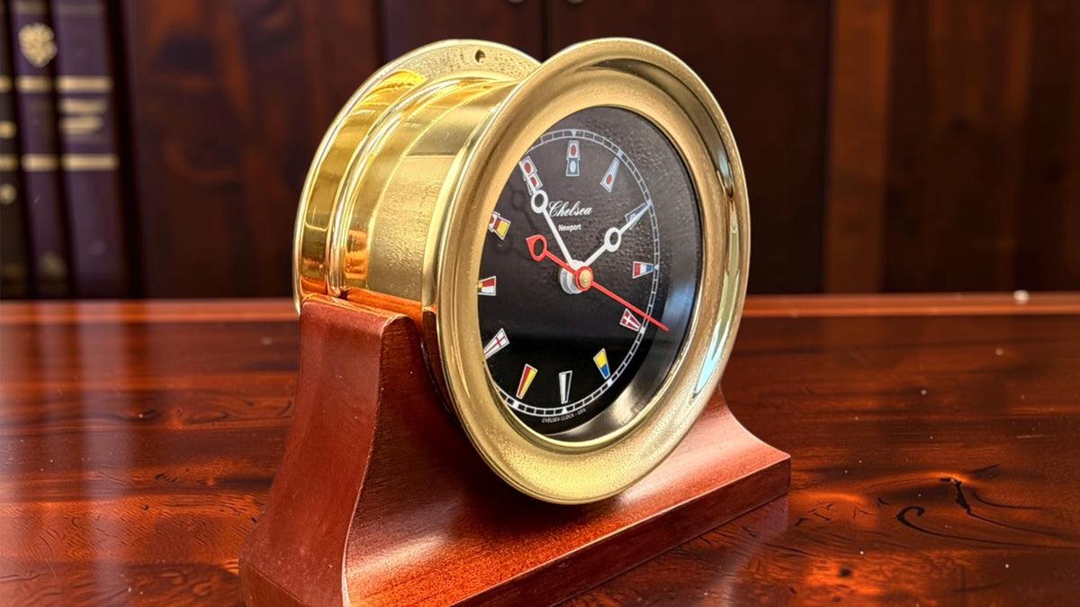 Chelsea Newport brass nautical clock angled in its mahogany-tone wood cradle